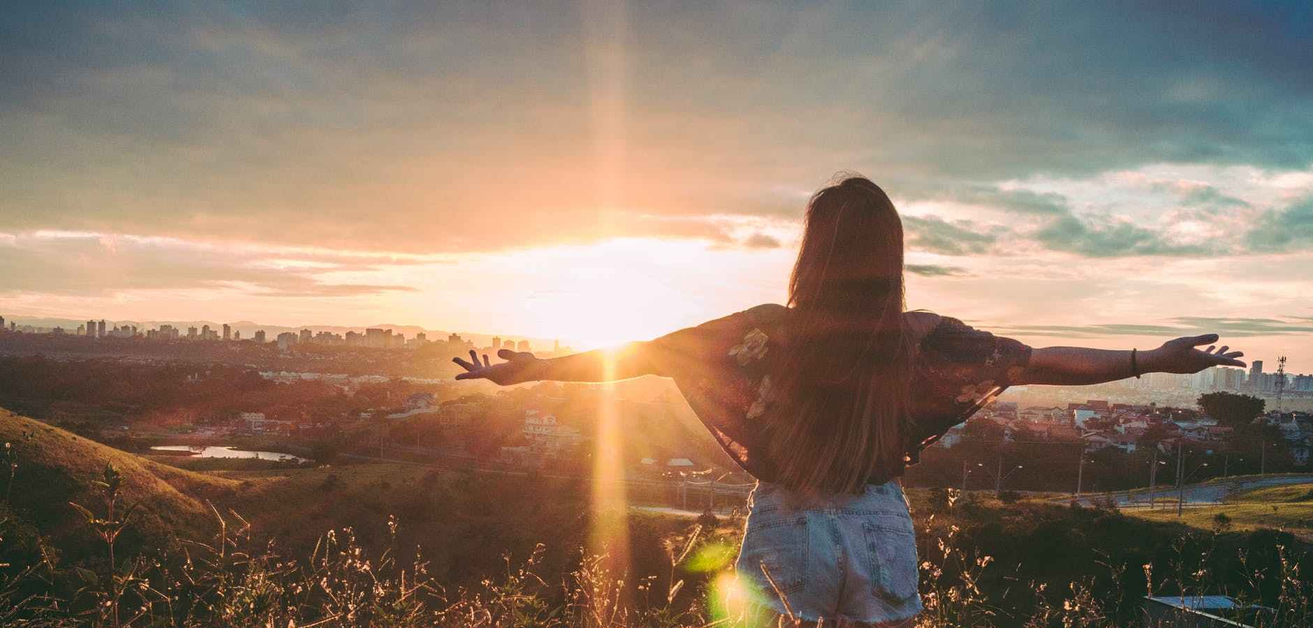 woman stands on mountain over field under cloudy sky at sunrise